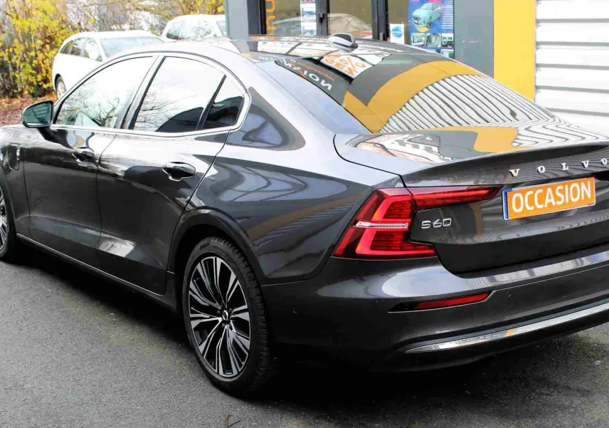 Vue 3/4 arrière droite d'une Volvo S60 gris métal 2024 avec jantes stylées et plaque "OCCASION" visible.
