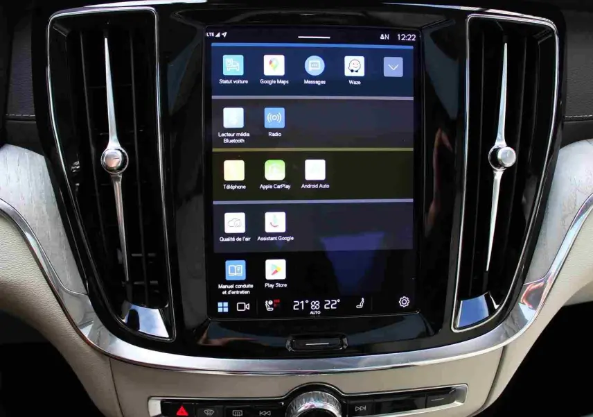 Écran tactile central avec interface multimédia, entouré de grilles d'aération chromées dans l'habitacle beige d'une Volvo S60 2024.