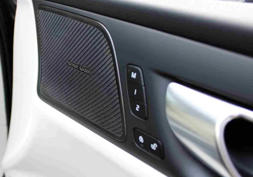 Gros plan sur la porte intérieure côté gauche du Volvo S60 gris métal 2024, avec haut-parleur Harman Kardon et commandes mémoire siège.
