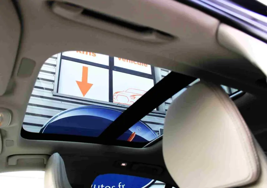 Vue intérieure du toit ouvrant panoramique d'une Volvo S60 gris métal 2024, avec appuie-tête beige visible.