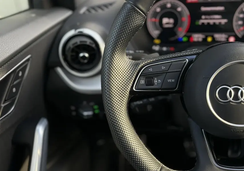 Gros plan sur le volant cuir perforé à 3 branches et le tableau de bord numérique de l'Audi Q2 35 TDI 150 S-Line 2025.