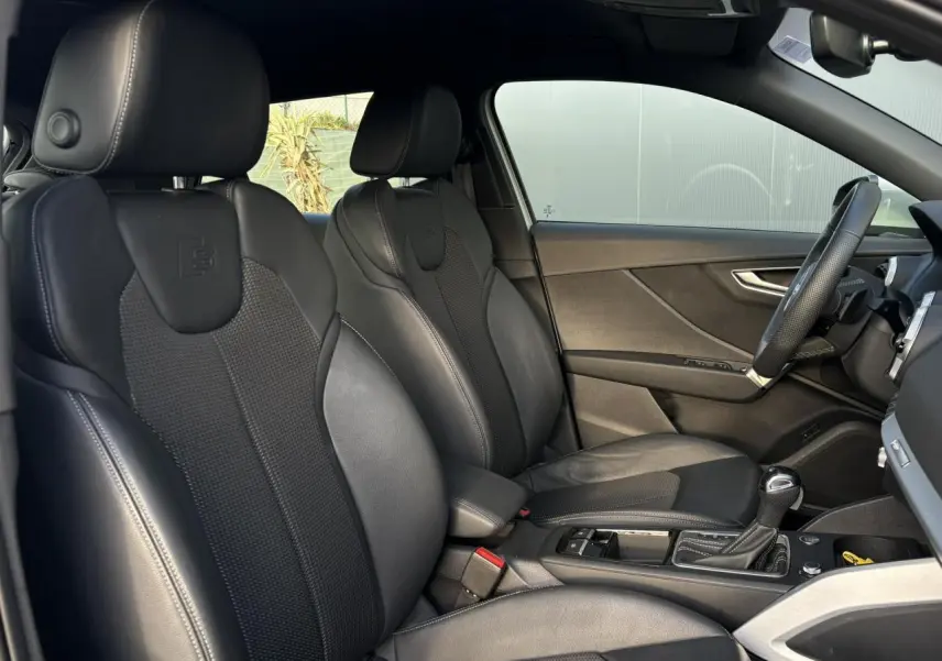 Vue intérieure côté conducteur de l'Audi Q2 35 TDI S-Line 2025 avec sièges sport cuir/tissu noirs et volant cuir.