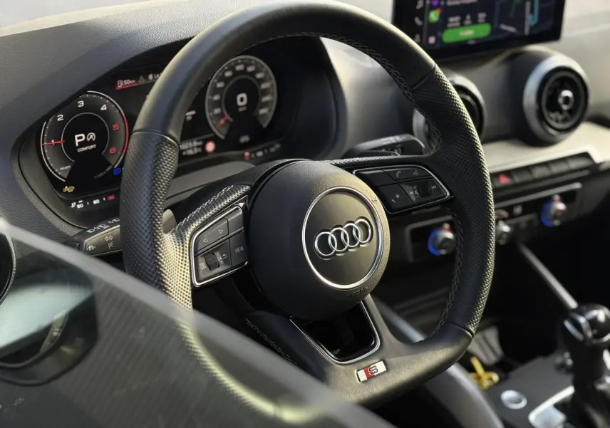 Vue rapprochée du volant sport en cuir noir avec logo Audi et tableau de bord numérique du Q2 35 TDI 2025.