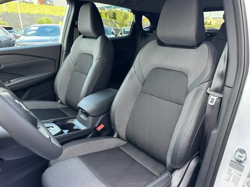 Vue intérieure côté conducteur du Nissan Qashqai Hybrid e-POWER 2025, sièges tissu gris avec surpiqûres contrastées.