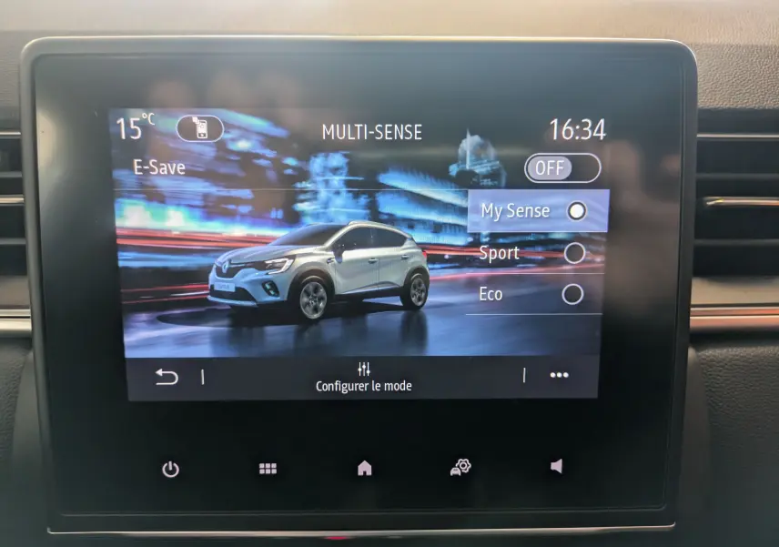 Écran tactile du système multimédia montrant un Renault Captur gris Highland en 3/4 avant sur fond urbain nocturne.