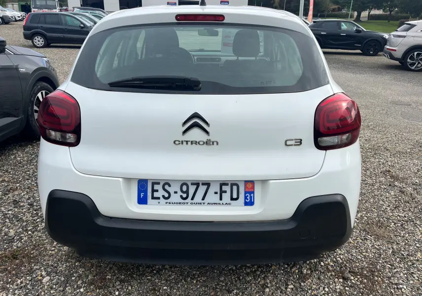 Vue arrière d'une Citroën C3 blanche de 2017 avec feux rouges et pare-chocs noir sur parking gravillonné.