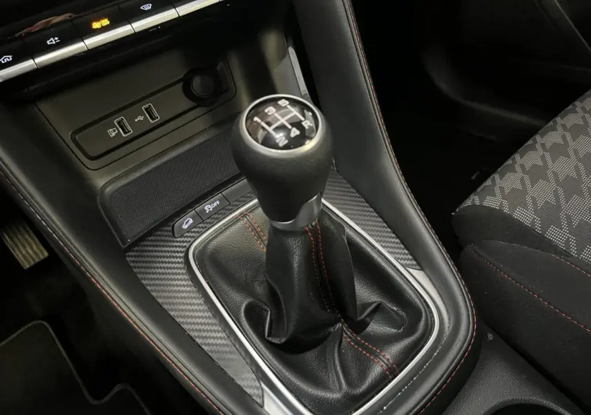 Le levier de vitesses manuel noir avec surpiqûres rouges de la MG ZS 1.5L VTi Tech 2022, entouré d'un habillage effet carbone.