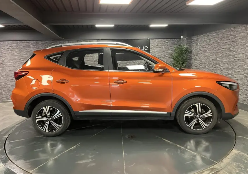 Vue latérale côté gauche du MG ZS orange 2022 avec jantes alliage 17 pouces Typhoon et barres de toit argentées.