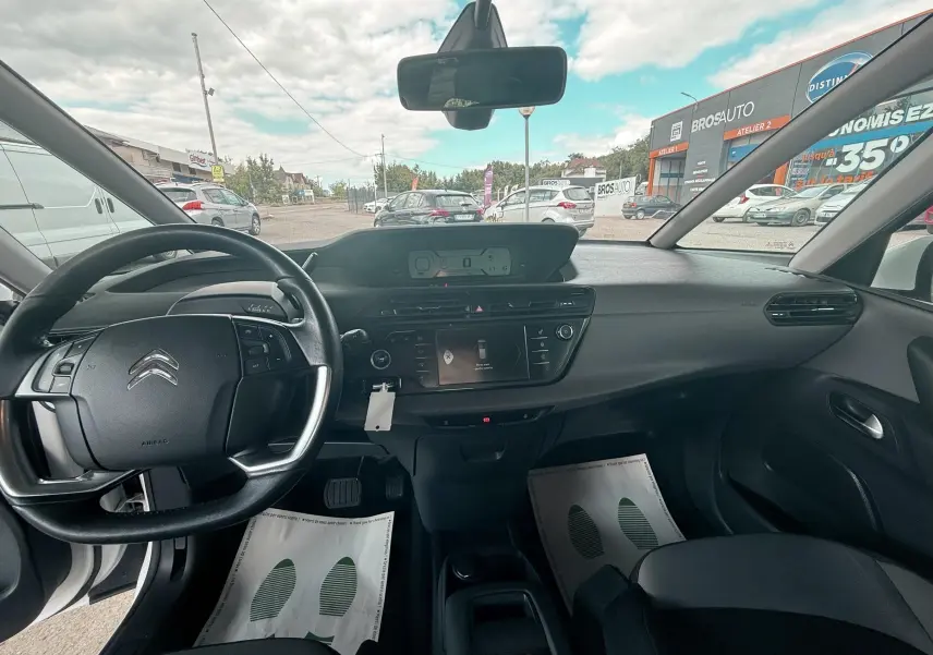 Vue intérieure avant du Citroën C4 Picasso blanc 2014, tableau de bord et volant avec commandes intégrées visibles.