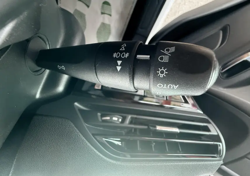 Gros plan sur la commande des feux et clignotants à gauche du volant dans l’habitacle d’une Citroën C4 Picasso blanc 2014.