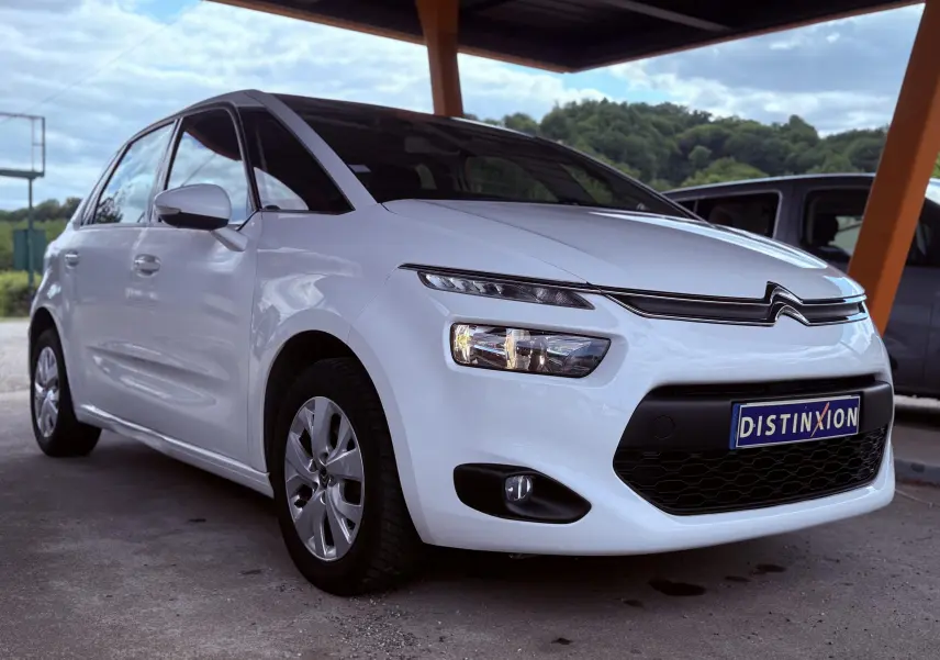 Vue 3/4 avant gauche d'une Citroën C4 Picasso blanche de 2014 avec phares allumés et calandre noire distinctive.