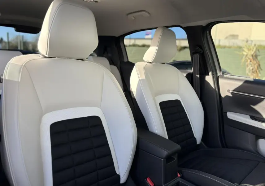 Vue intérieure sur les sièges avant bicolores blanc et noir du Citroën C3 Aircross Hybrid 2025, avec accoudoir central noir.