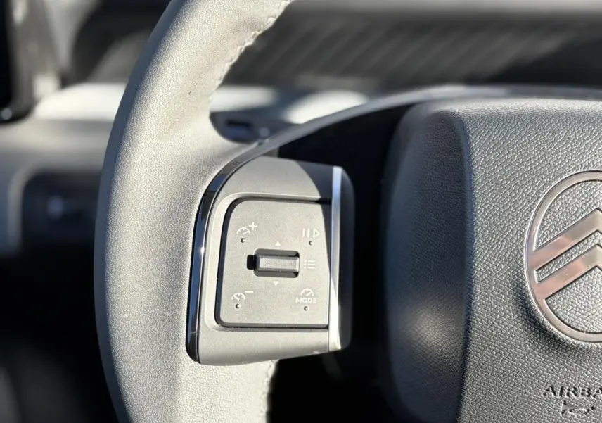 Gros plan sur les commandes gauche du volant gris du Citroën C3 Aircross Hybrid 2025 avec logo chrome visible.