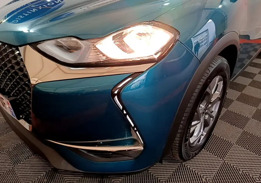 Gros plan sur l'avant droit bleu du DS3 Crossback 2020 avec phare allumé et calandre distinctive en losange.