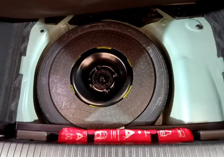 Vue plongeante sur la roue galette noire dans le coffre bleu clair du DS3 Crossback avec trousse de secours rouge.