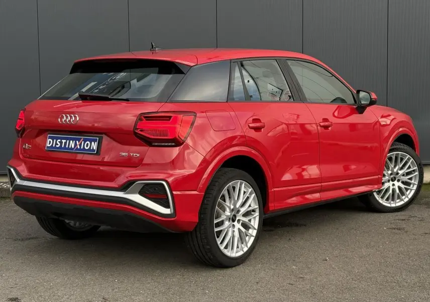 Audi Q2 35 TDI S-Line rouge vue 3/4 arrière droit, avec jantes alliage et feux arrière LED distinctifs.