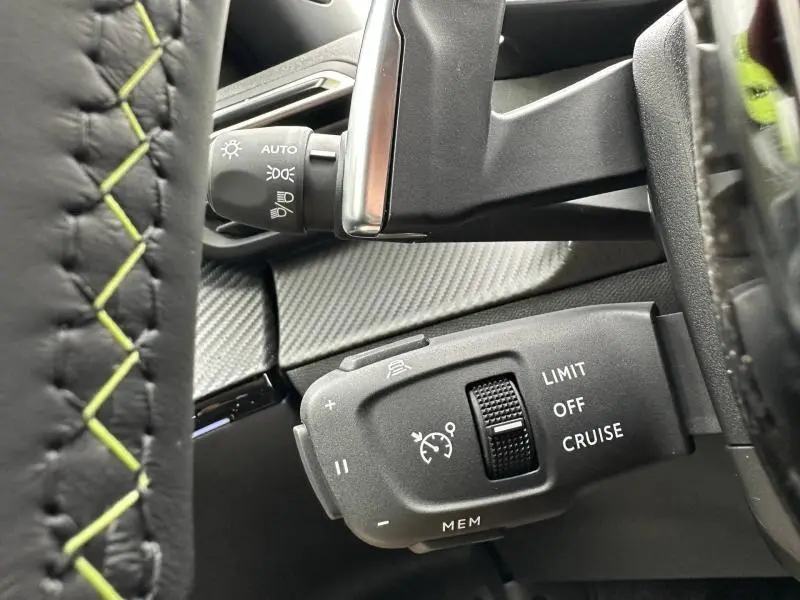 Gros plan sur la commande de régulateur de vitesse du Peugeot 2008 gris hybride 2025, avec volant cuir et surpiqûres vertes.