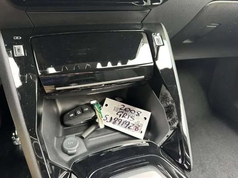 Gros plan sur la console centrale noire brillante du Peugeot 2008 gris 2025 avec clés et prise 12V visibles.
