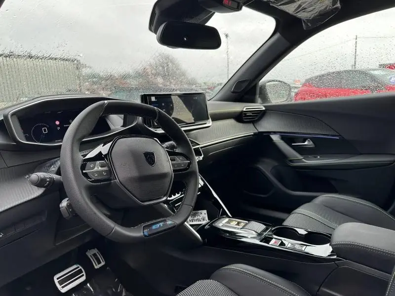 Vue intérieure côté conducteur du Peugeot 2008 gris 2025, mettant en valeur le volant GT et l'écran tactile central.