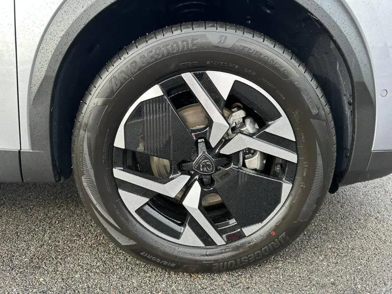 Gros plan sur la roue avant droite du Peugeot 2008 gris 1.2 Hybrid 145ch GT e-DCS6 avec jante noire et argentée distinctive.