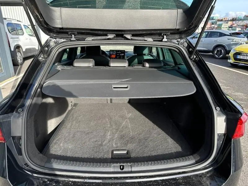 Coffre ouvert vu de l'arrière d'une SEAT LEON ST 1.5 eTSI Hybrid noir minuit métallisé avec cache-bagages en place.