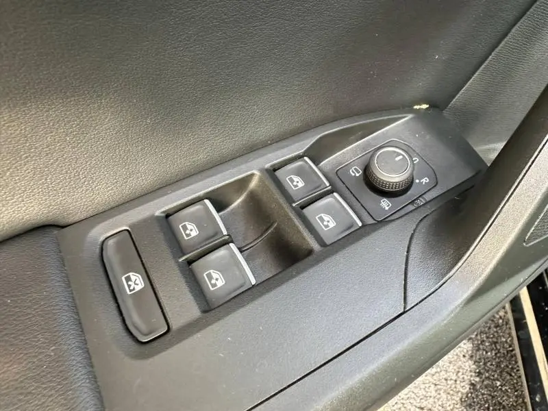 Gros plan sur les commandes de lève-vitres et réglages des rétroviseurs côté conducteur d'une SEAT LEON ST noir Minuit Métallisée 2025.