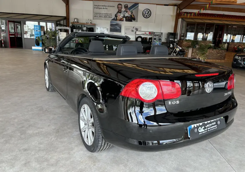 Volkswagen EOS noir en cabriolet vu de l'arrière droit dans un showroom avec sièges en cuir gris.