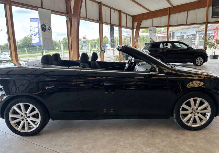 Volkswagen EOS cabriolet noir vu de profil côté gauche, intérieur découvert, jantes alliage visibles en showroom.