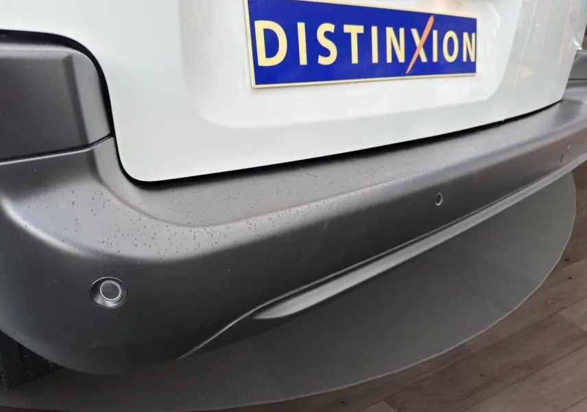 Gros plan sur le pare-chocs arrière noir d'un Peugeot Partner blanc avec capteurs de recul et plaque Distinxion.