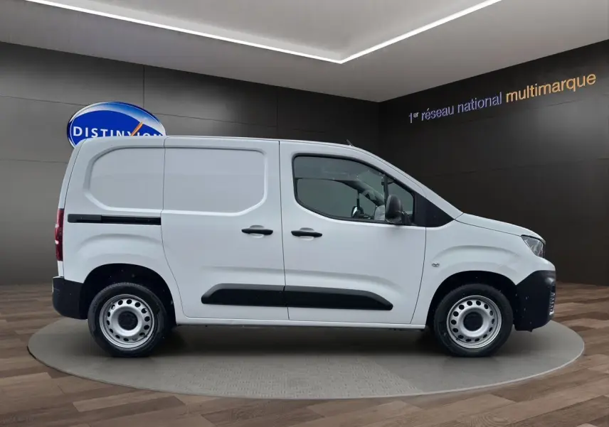 Profil côté gauche d'un utilitaire Peugeot Partner blanc 2022 avec protections noires et jantes acier en showroom.