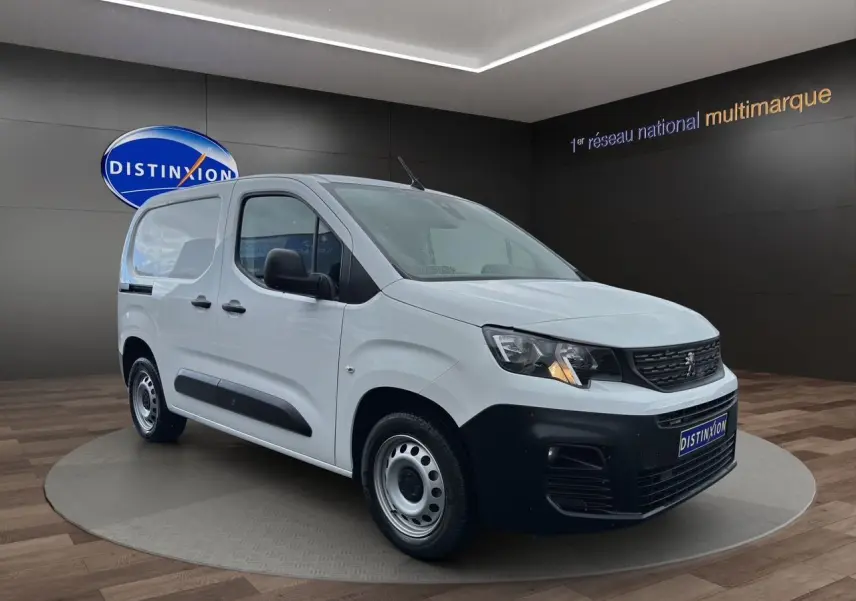Vue 3/4 avant droite d'un Peugeot Partner blanc avec pare-chocs noir et jantes acier en showroom.