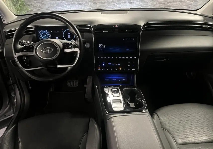 Intérieur du Hyundai Tucson 2023 vu de face, tableau de bord noir avec écran tactile central et volant cuir.