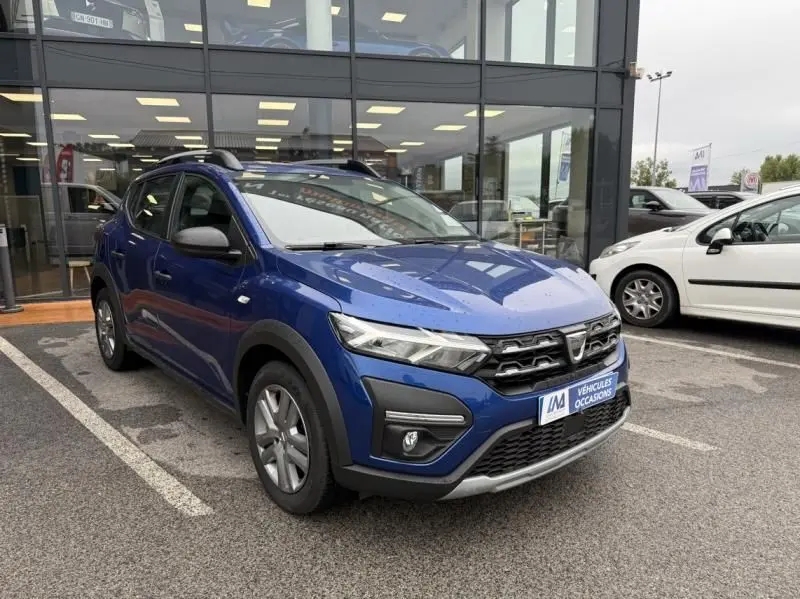 Vue 3/4 avant d'une Dacia Sandero Stepway bleu métal 2022 avec calandre noire et protections plastiques noires.