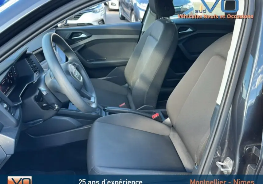 Vue intérieure côté conducteur de l'Audi A1 Sportback gris foncé, montrant sièges et tableau de bord modernes.