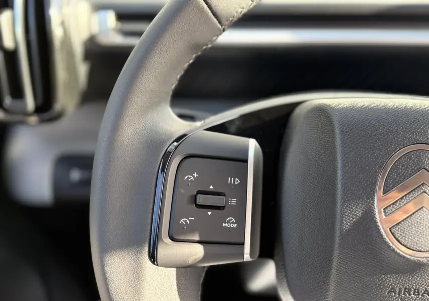 Gros plan sur le volant multifonctions gris clair du Citroën C3 Aircross Hybrid avec commandes de régulateur.