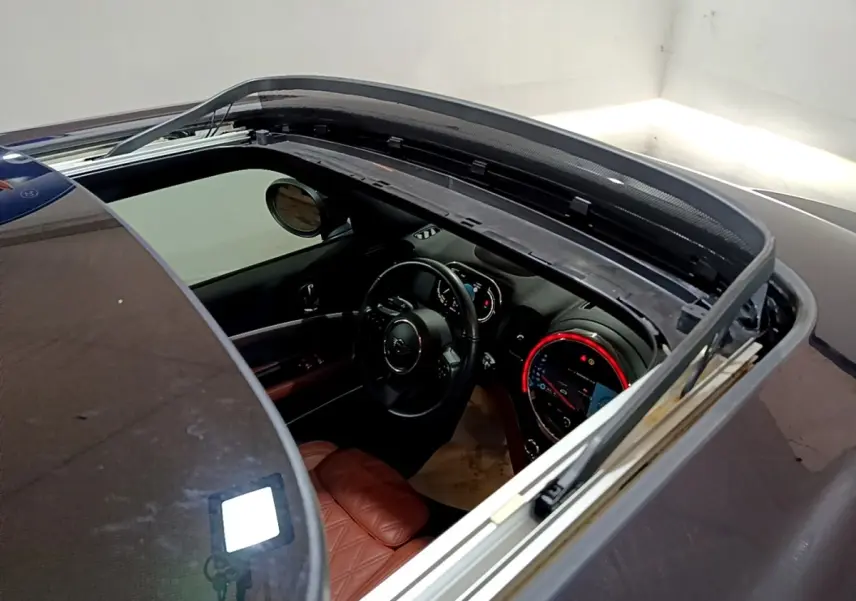 Vue plongeante sur l'intérieur d'une MINI Countryman bleu, toit ouvrant ouvert, volant cuir et tableau de bord éclairé.