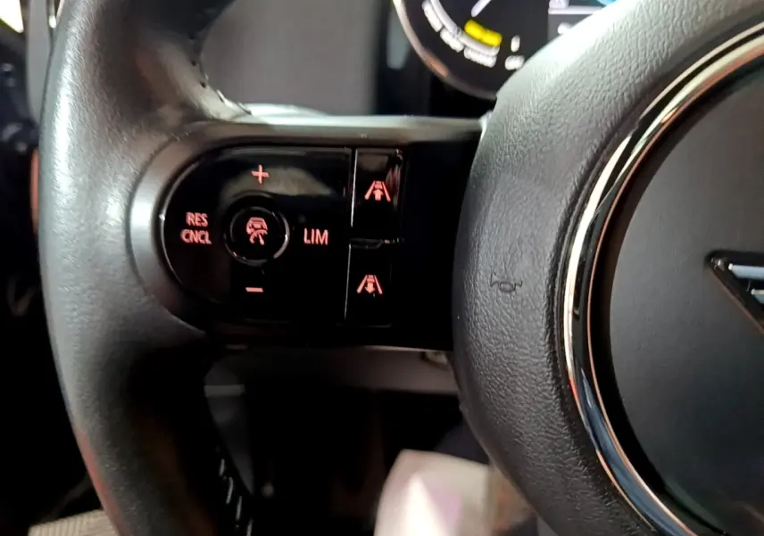Gros plan sur les commandes de régulateur de vitesse à gauche du volant cuir du MINI Countryman Cooper SE bleu 2021.