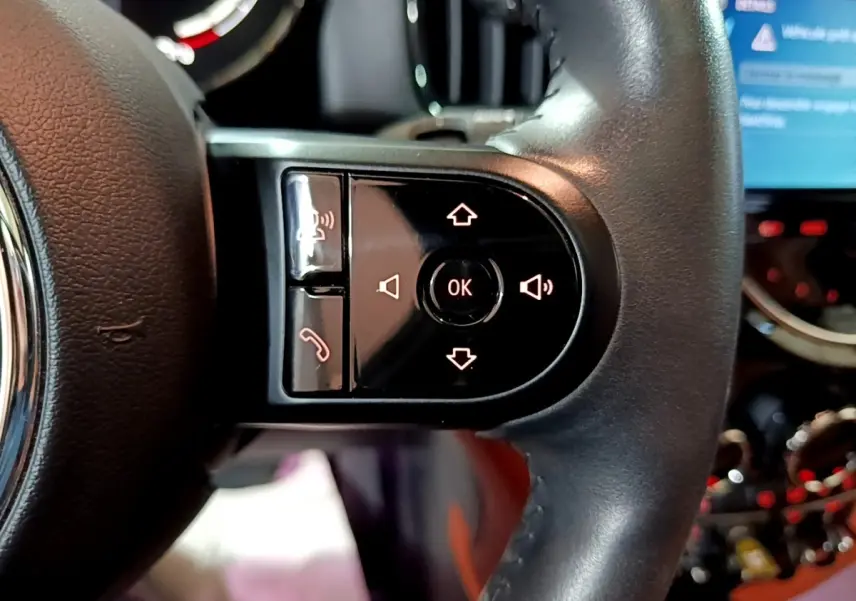 Gros plan sur les commandes au volant cuir noir de la MINI COUNTRYMAN hybride rechargeable 2021, avec écran tactile en arrière-plan.