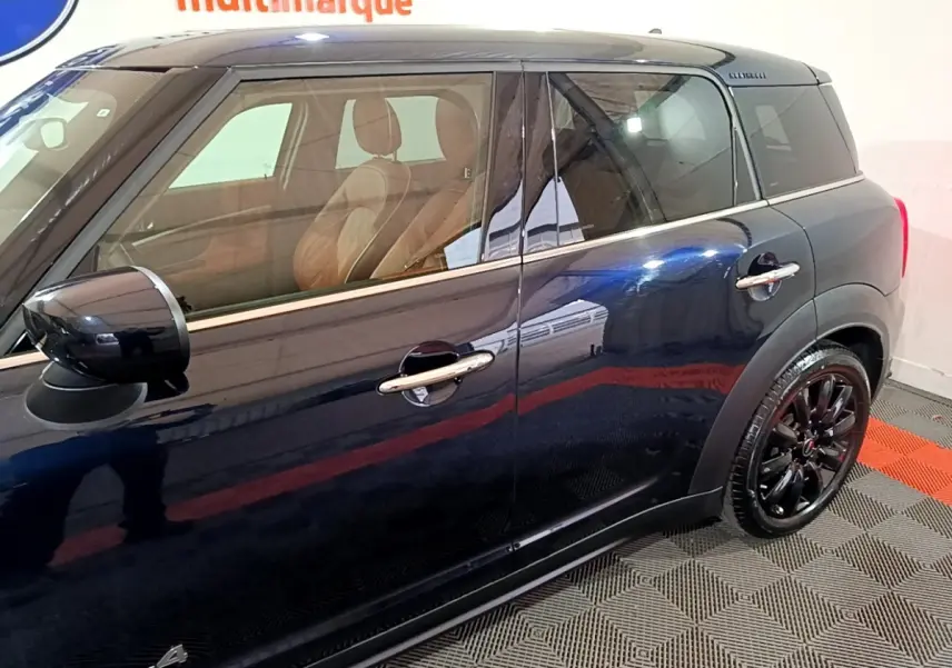 Vue latérale droite d'une MINI Countryman Cooper SE bleu foncé avec jantes noires et intérieur cuir marron visible.