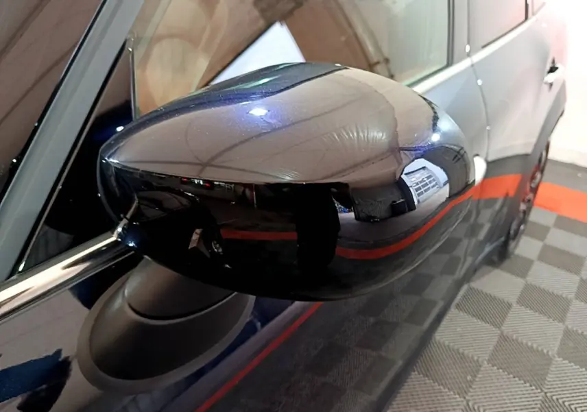 Rétroviseur côté gauche noir brillant d'une MINI Countryman hybride bleu, vue rapprochée sur fond intérieur showroom.