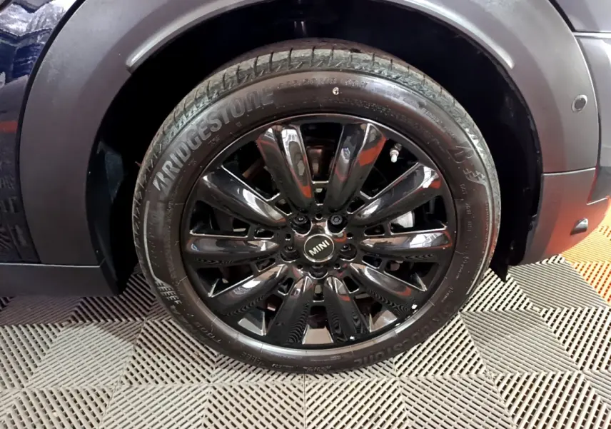 Gros plan sur la roue avant droite noire brillante du MINI Countryman Cooper SE bleu, avec pneu Bridgestone visible.