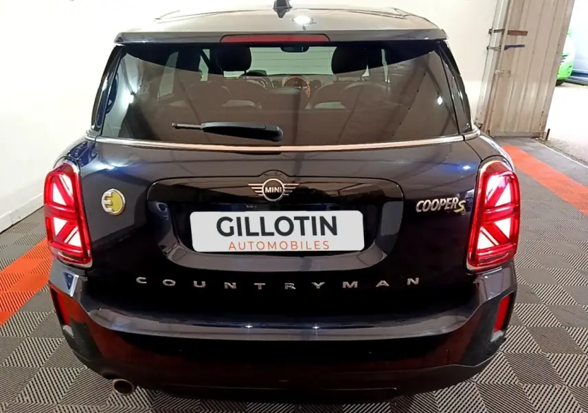 Vue arrière d'une MINI Countryman Cooper SE bleu avec feux arrière LED et logo électrique jaune sur le côté gauche.