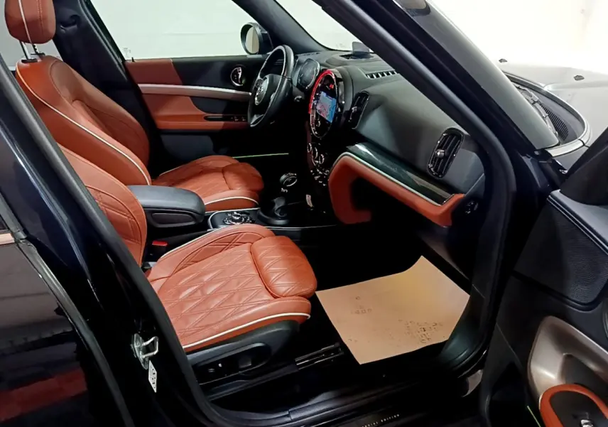 Intérieur avant droit d'une MINI Countryman bleu, sièges cuir marron matelassé et tableau de bord moderne.