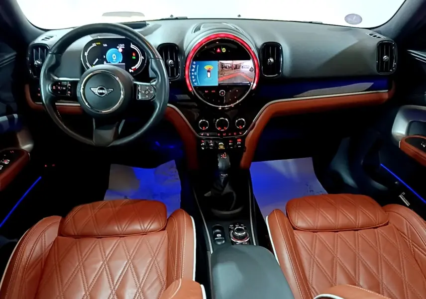 Vue intérieure avant du MINI Countryman Cooper SE avec sièges en cuir marron et tableau de bord numérique éclairé.