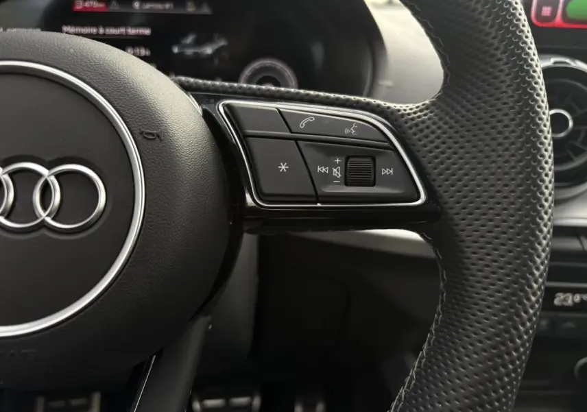 Gros plan sur le volant cuir perforé côté droit de l'Audi Q2 35 TDI 150 S-Tronic S-Line avec commandes multimédia intégrées.