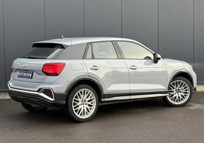 Audi Q2 35 TDI S-Line gris Flèche vue 3/4 arrière droit, avec jantes alliage et feux arrière LED distinctifs.