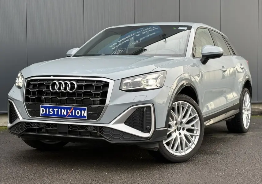 Audi Q2 35 TDI S-Line gris Flèche vue 3/4 avant droit, avec calandre noire et jantes alliage multibranches.