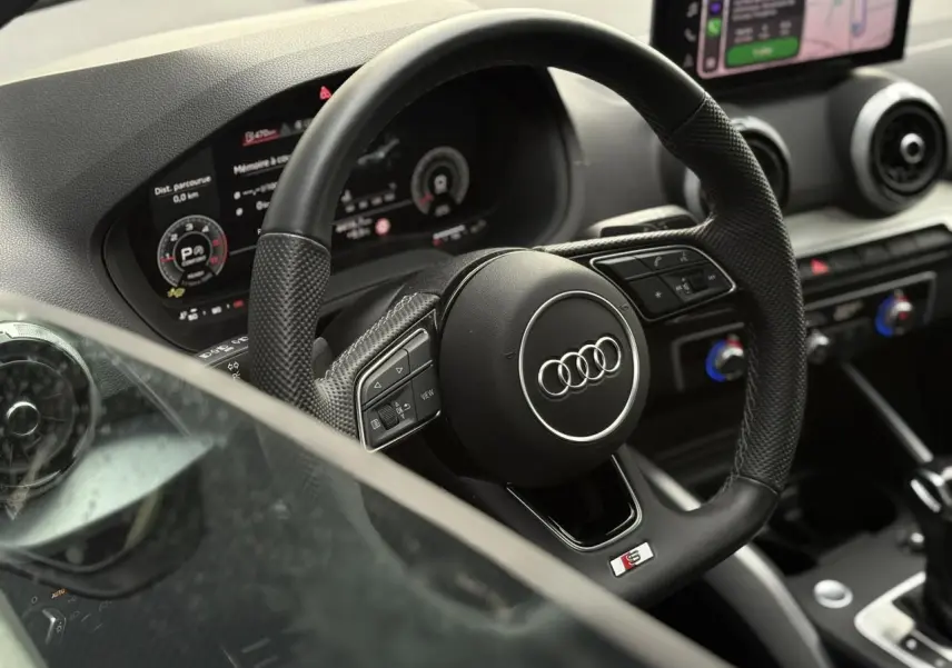 Vue rapprochée du volant sport en cuir noir avec logo Audi et tableau de bord numérique du Q2 35 TDI S-Line.