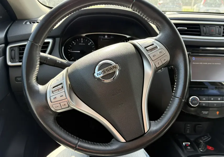 Vue rapprochée du volant en cuir noir du Nissan X-Trail 2016, avec commandes intégrées et tableau de bord partiel visible.
