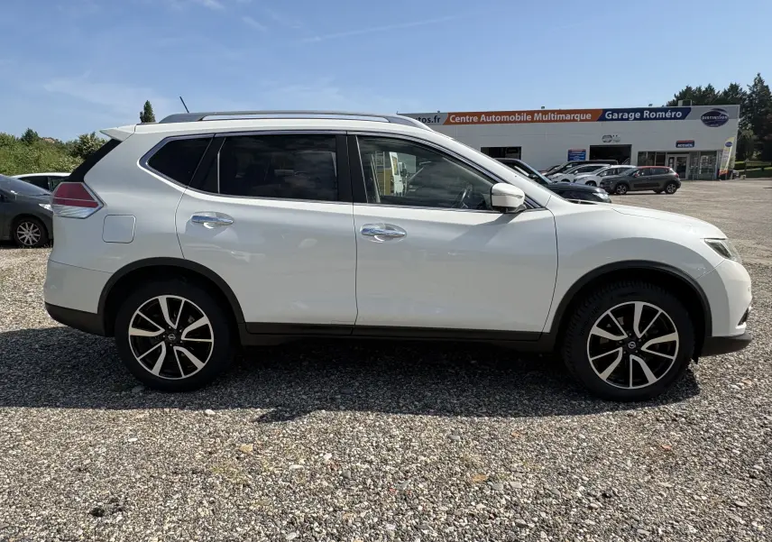 Vue de profil côté gauche d'un Nissan X-TRAIL 2016 blanc, version White Edition 7 places avec jantes alliage noires et argentées.